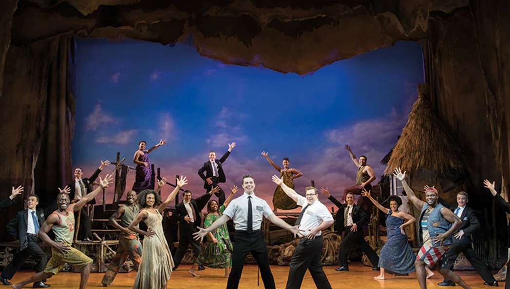 Cast performing a scene from The Book of Mormon musical on stage.