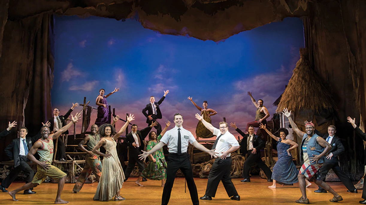 Cast performing a scene from The Book of Mormon musical on stage.