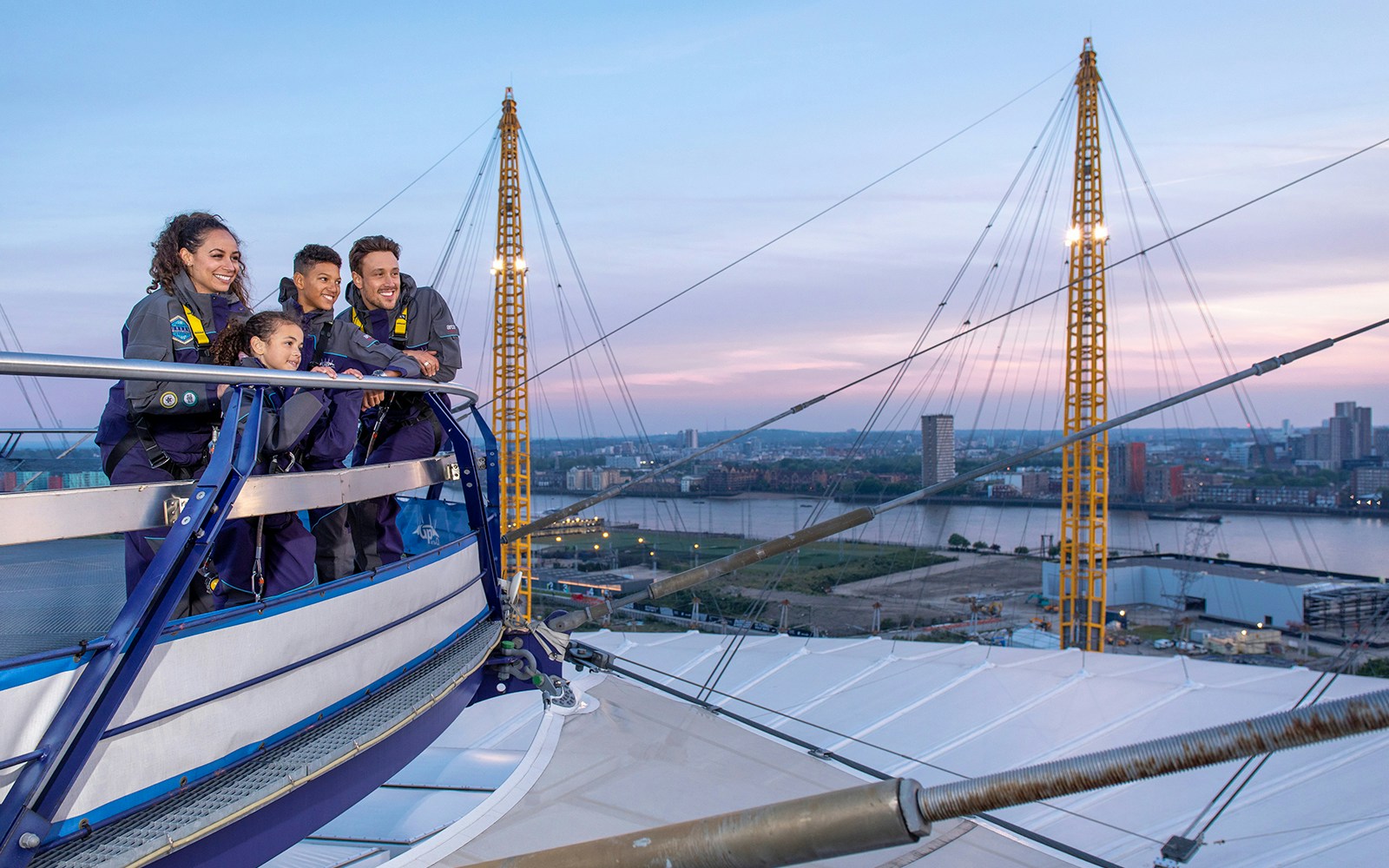 Climbers on top of The O2 in London during sunset, overlooking the city skyline.