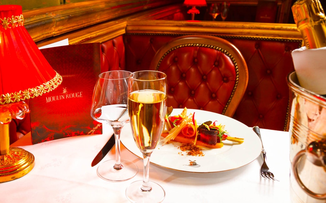 Dinner setting at Moulin Rouge cabaret in Paris with champagne and gourmet dish.