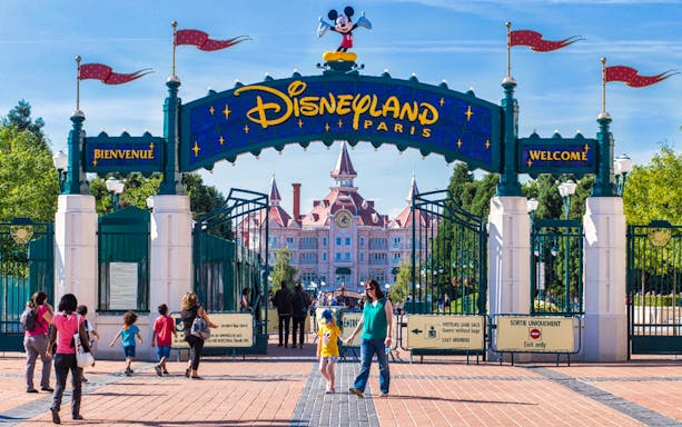 Entrance to Disneyland Paris with visitors walking through gates.