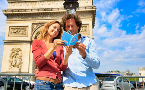 Couple reading Paris Pass guidebook in front of Arc de Triomphe, Paris.
