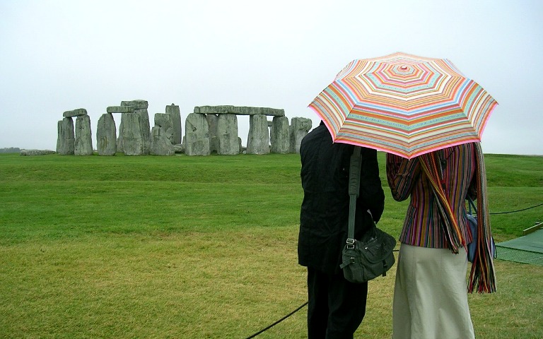 Visitors with umbrella viewing Stonehenge on a cloudy day.