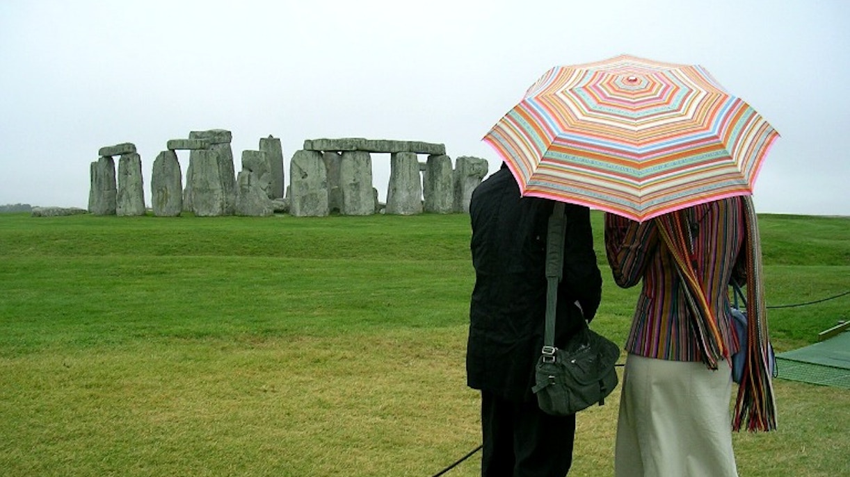 Visitors with umbrella viewing Stonehenge on a cloudy day.
