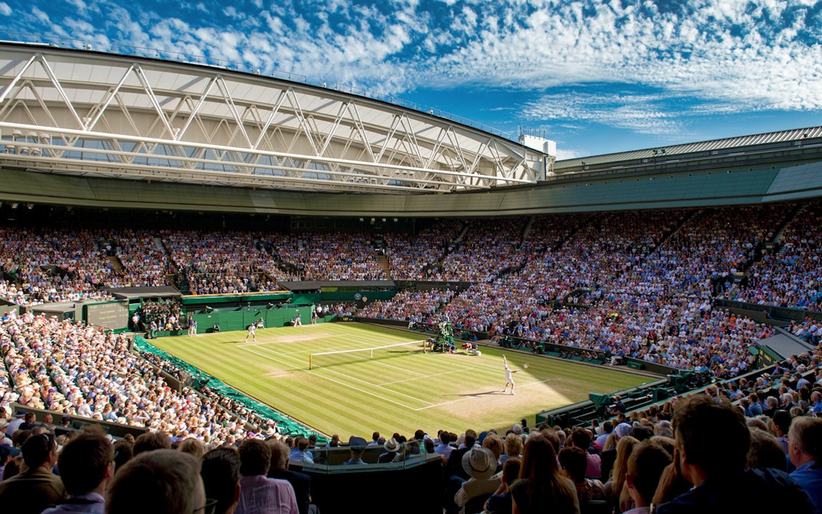 Wimbledon Centre Court during a tennis match, with a full crowd under a clear sky.