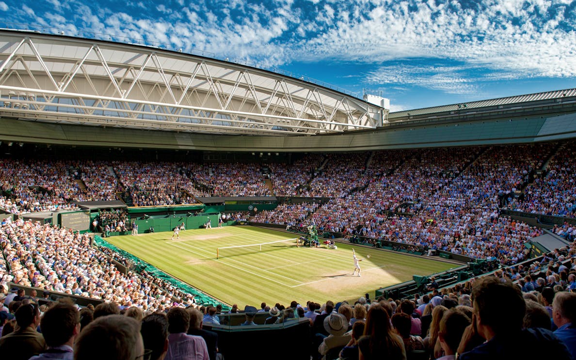 Wimbledon Centre Court during a tennis match, with a full crowd under a clear sky.