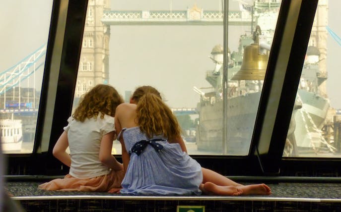 Two people sitting inside a boat with a view of Tower Bridge in London.