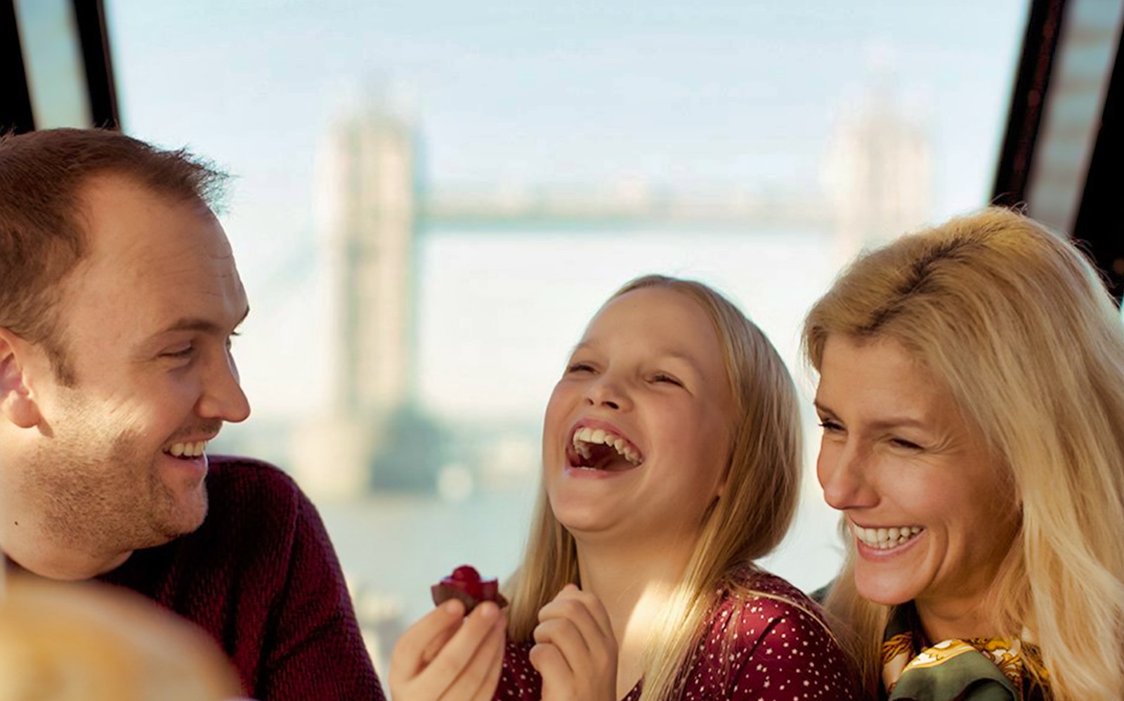 Family enjoying afternoon tea on a cruise with Tower Bridge in the background.