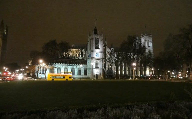 Westminster Abbey illuminated at night with a London tour bus in the foreground.