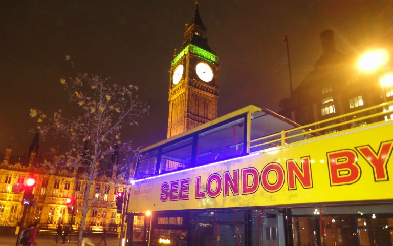 Open-top bus tour passing Big Ben at night in London.