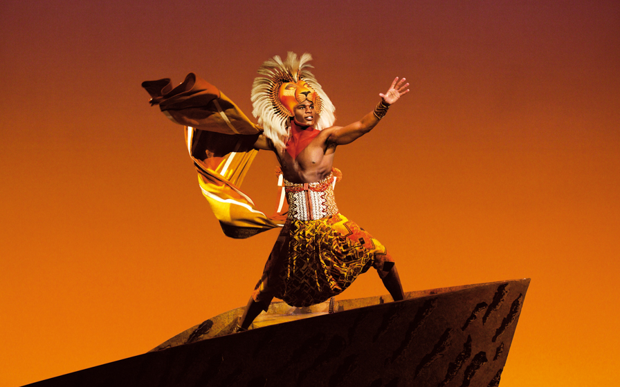 Performer in vibrant costume on stage during The Lion King musical.