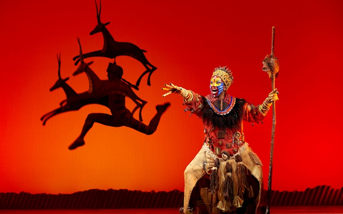 Performer in vibrant costume on stage during The Lion King musical.