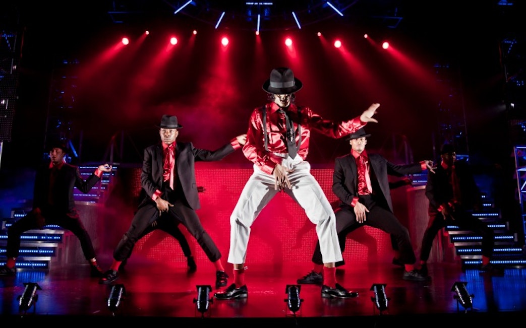 Performers dancing on stage in Thriller Live show with red lighting.