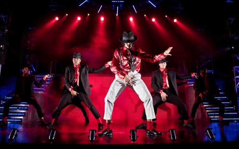 Performers dancing on stage in Thriller Live show with red lighting.