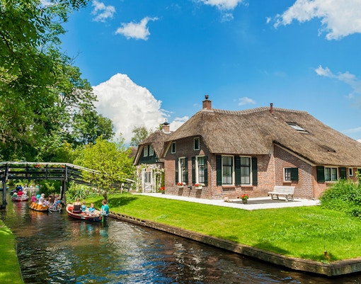 Small group boating through Giethoorn canal past traditional thatched house.
