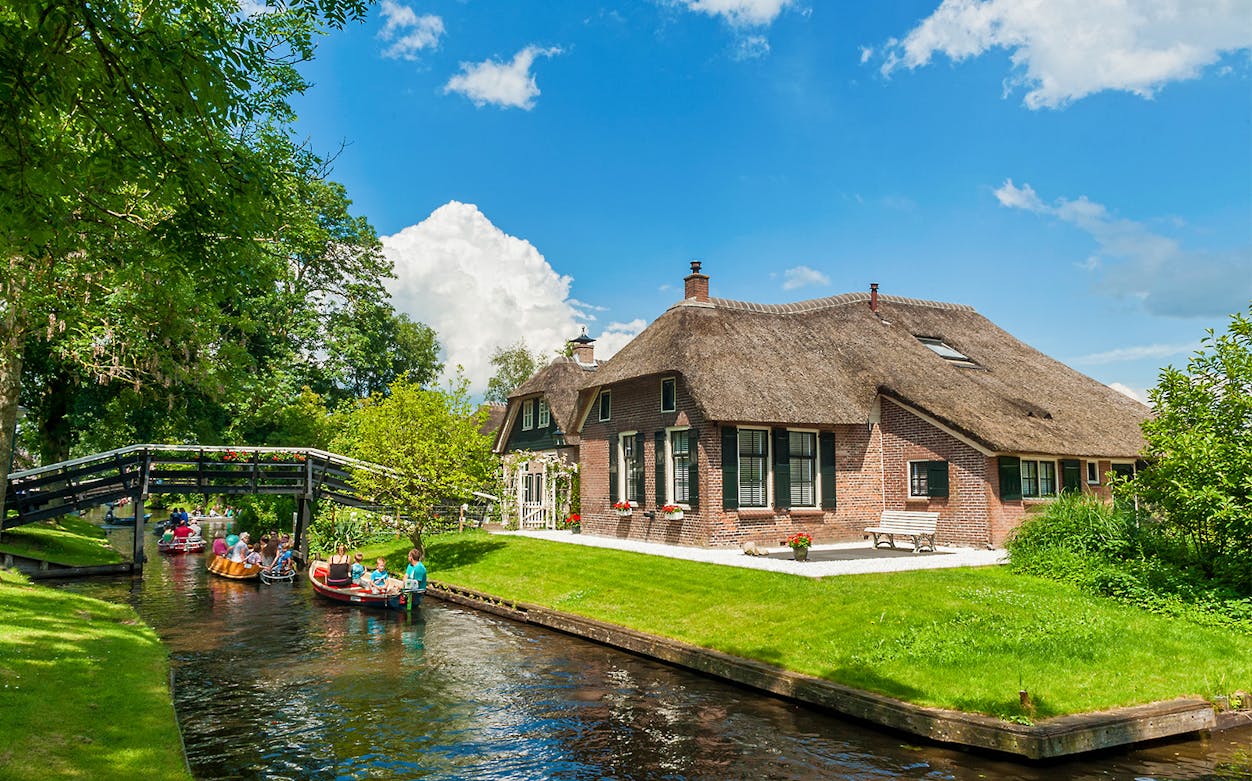 Small group boating through Giethoorn canal past traditional thatched house.