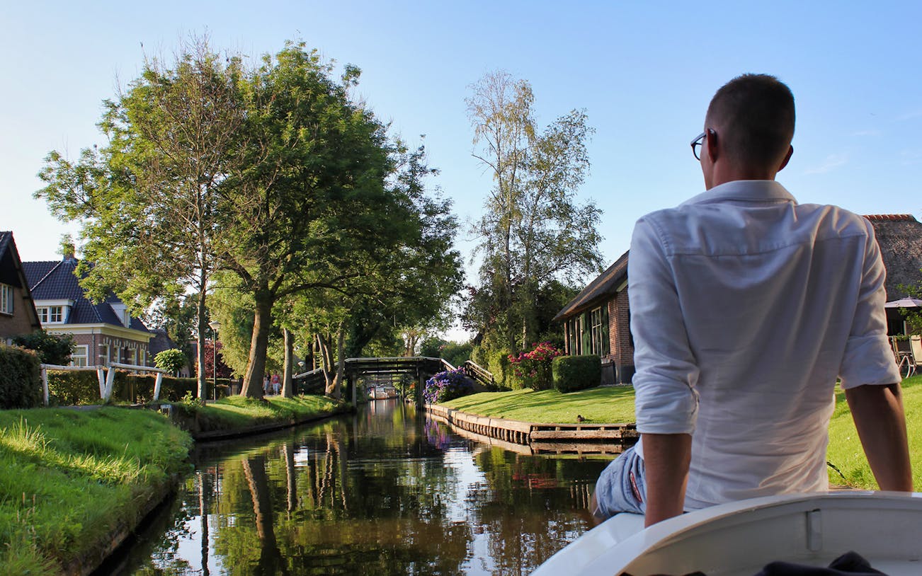 Small group boat tour through Giethoorn canal with scenic views of trees and houses.