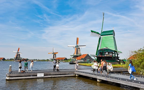 People walking on a boardwalk near traditional windmills in Zaanse Schans, Netherlands.
