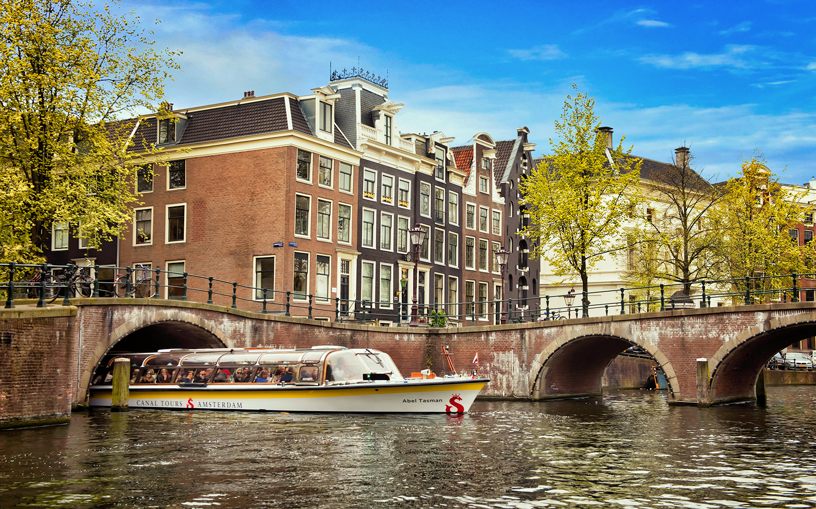 Canal boat tour passing under a bridge in Amsterdam, part of the Volendam, Edam, and Windmills Tour.