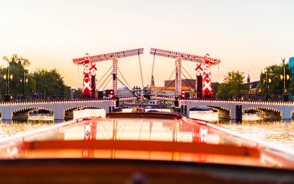 Evening view of the illuminated Magere Brug during a canal cruise in Amsterdam.