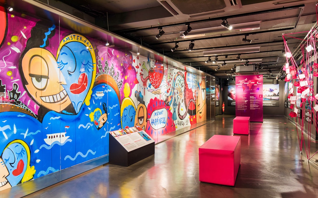 Colorful graffiti art at Body Worlds Amsterdam exhibit, featuring vibrant characters and "Instant Happiness" text.