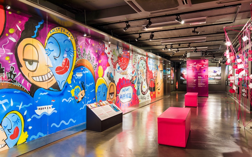 Colorful graffiti art at Body Worlds Amsterdam exhibit, featuring vibrant characters and "Instant Happiness" text.