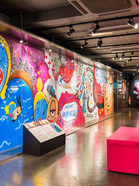 Colorful graffiti art at Body Worlds Amsterdam exhibit, featuring vibrant characters and "Instant Happiness" text.