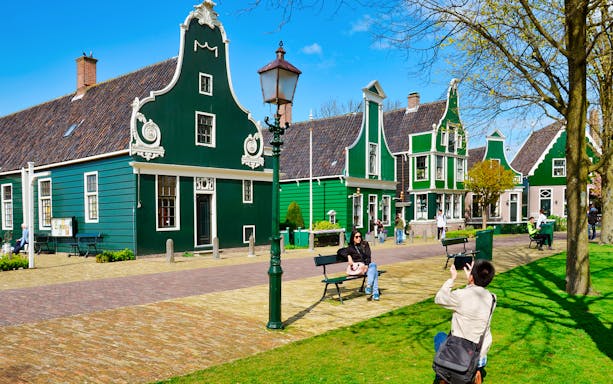 Traditional green wooden houses in Zaanse Schans, Netherlands, with tourists exploring the area.
