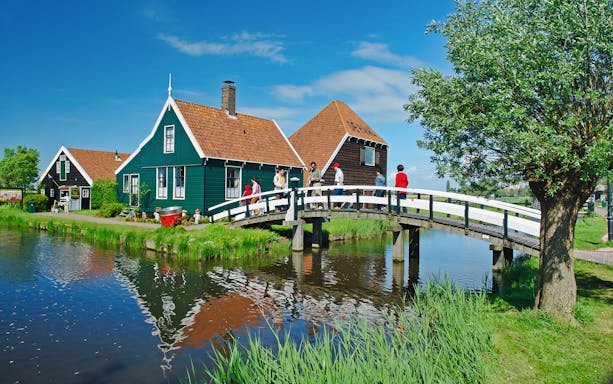 Visitors crossing a bridge at Zaanse Schans, Netherlands, with traditional Dutch houses in the background.