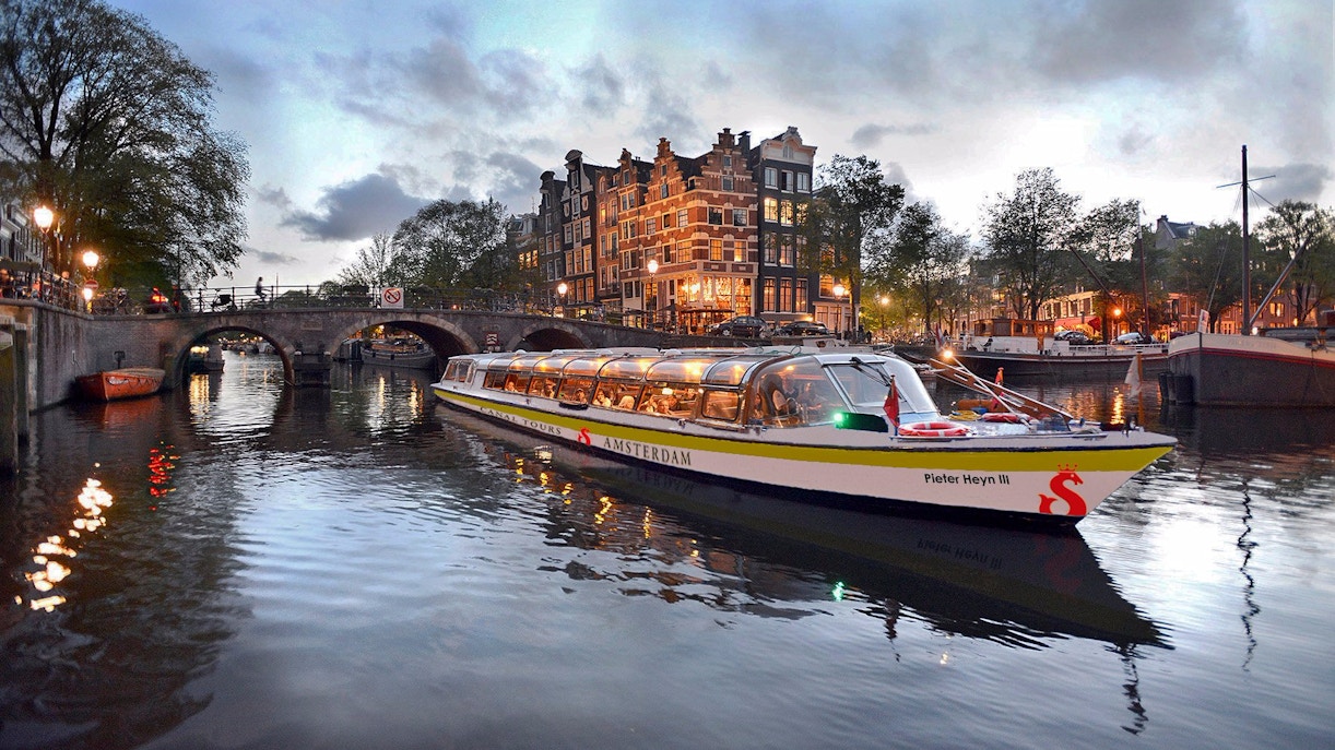 Canal boat cruising Amsterdam's illuminated waterways at dusk.