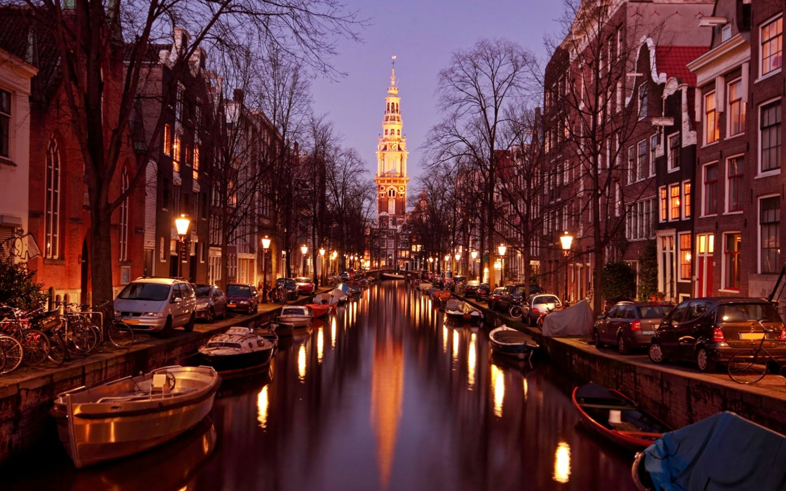 Canal view with boats and illuminated church tower in Amsterdam during evening cruise.