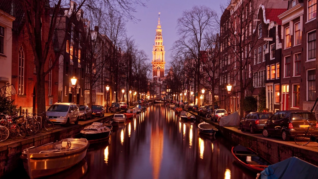 Canal view with boats and illuminated church tower in Amsterdam during evening cruise.