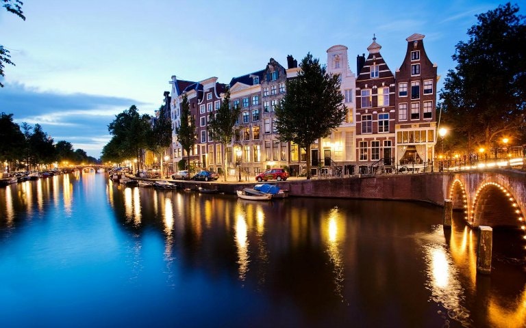 Evening canal cruise in Amsterdam with illuminated bridges and historic buildings.