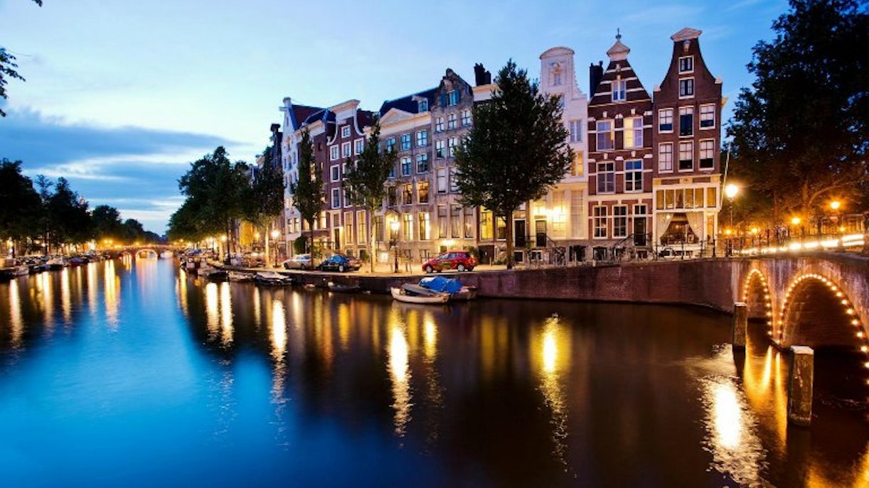 Evening canal cruise in Amsterdam with illuminated bridges and historic buildings.