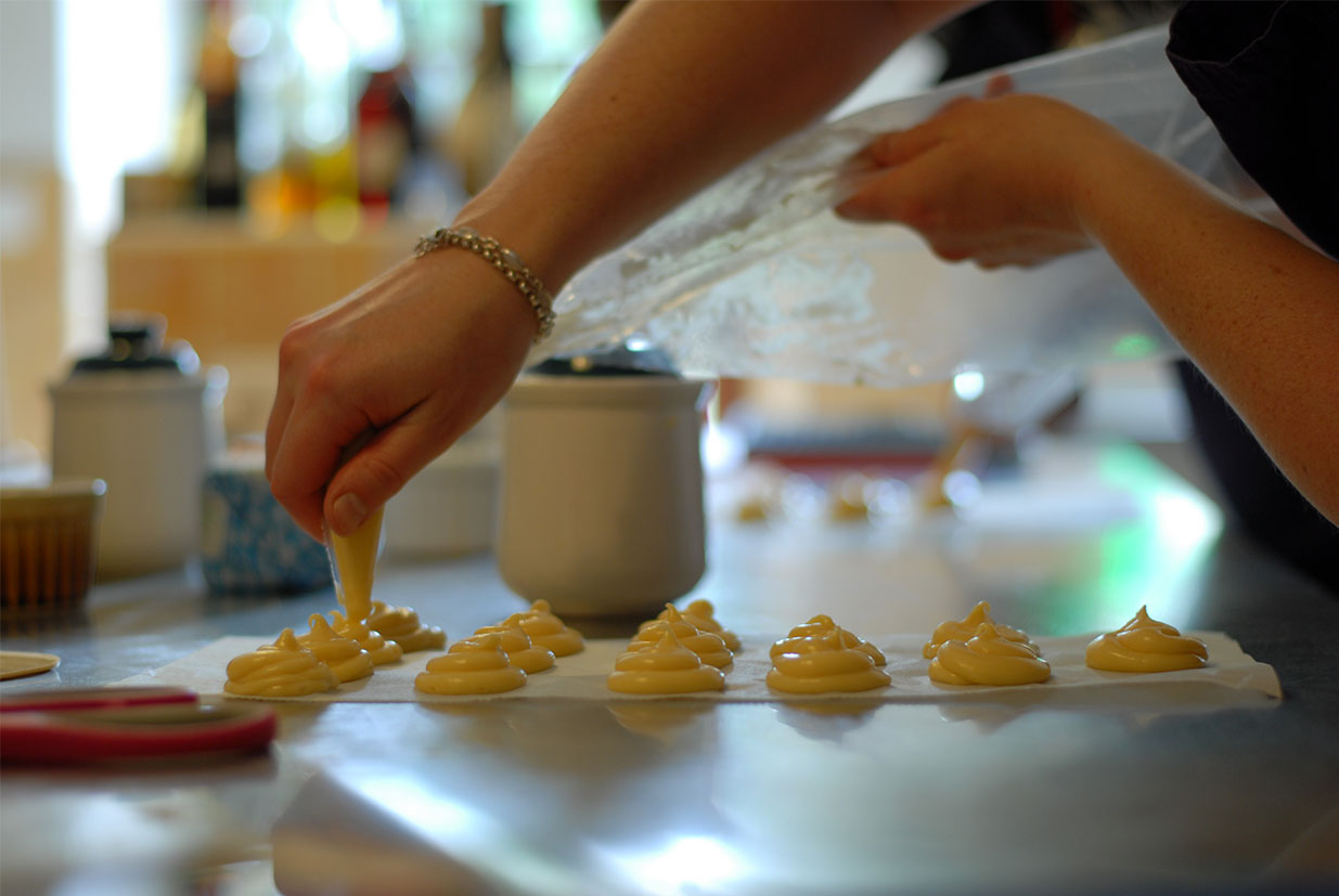 Piping choux pastry onto a baking sheet during a French pastry cooking class.