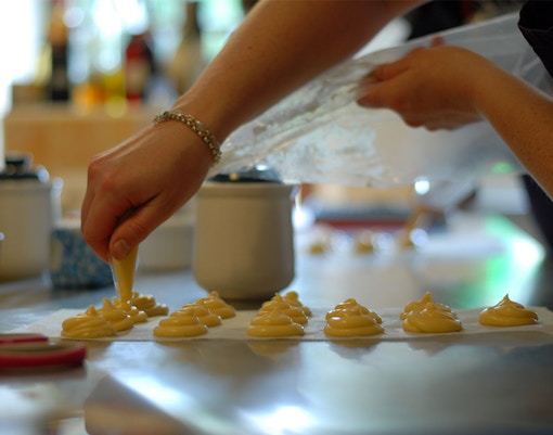 Piping choux pastry onto a baking sheet during a French pastry cooking class.
