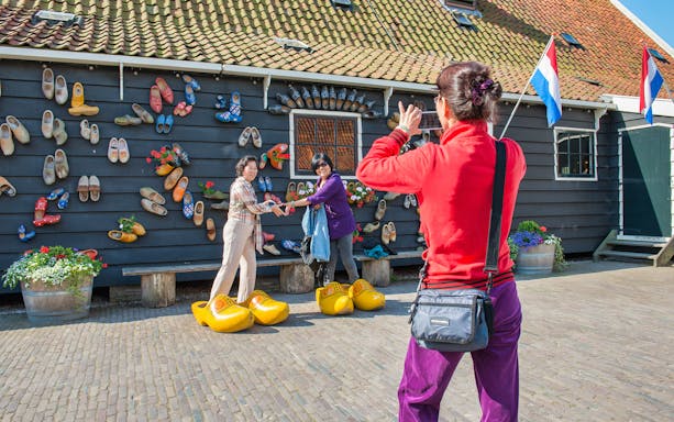 Visitors posing with large wooden clogs at a traditional Dutch house in Zaanse Schans.