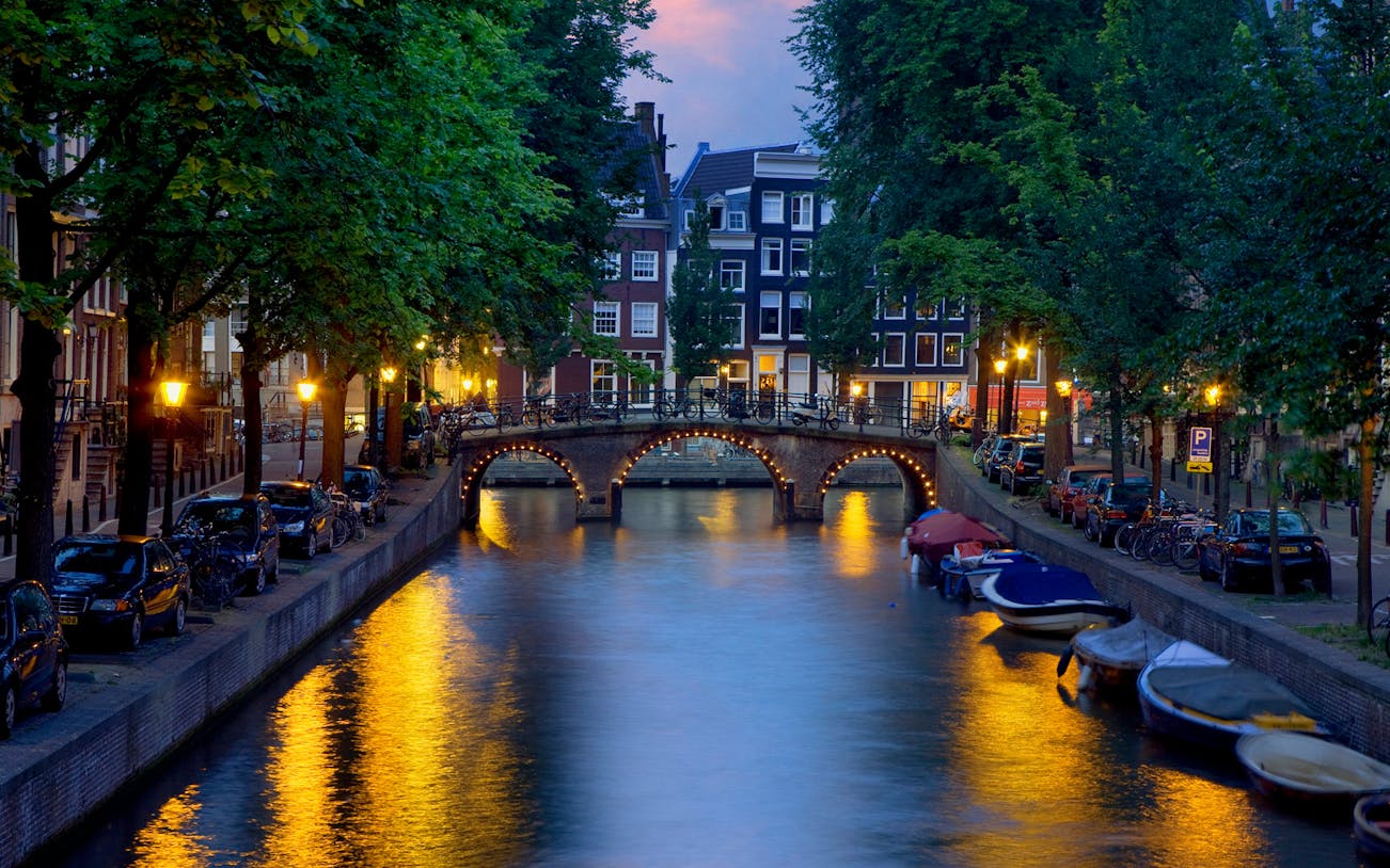 Amsterdam canal with illuminated bridge and boats at dusk.