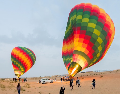 Hot air balloons preparing for flight in Dubai desert with tourists nearby.