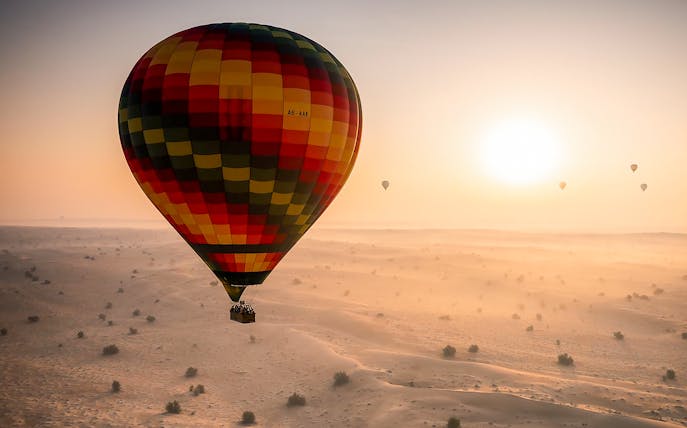Hot air balloon over Dubai desert at sunrise during tour with hotel transfers.