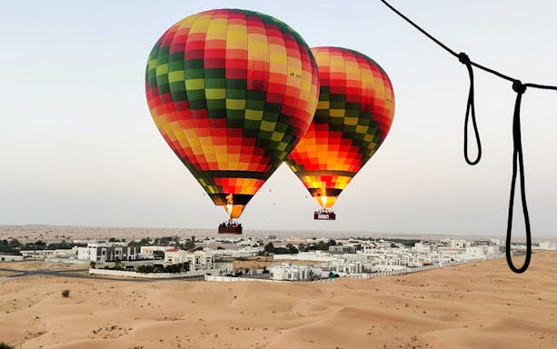 Hot air balloons over Dubai desert with cityscape in background.