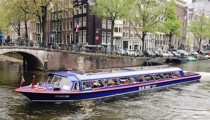 Amsterdam canal cruise boat near historic buildings, part of Rembrandt House Museum and canal tour combo.