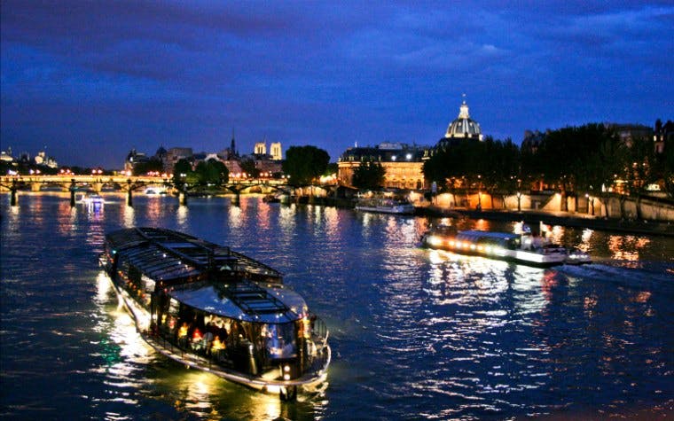 Eiffel Tower illuminated at night with Seine River cruise boat in Paris.