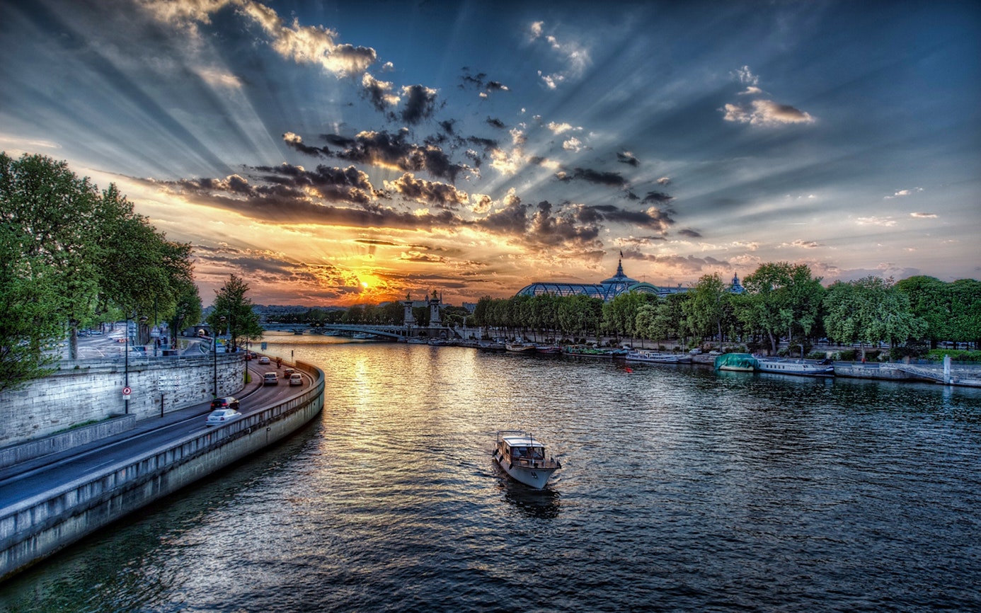 Seine River at sunset with boat, Paris cityscape in background.