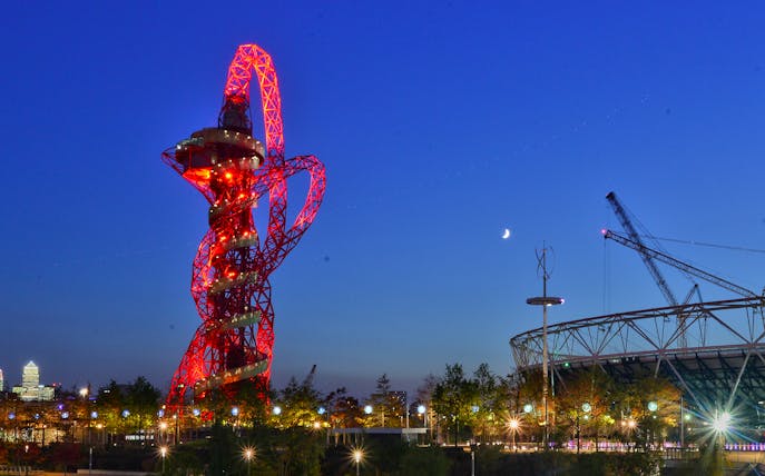 ArcelorMittal Orbit illuminated at night with London skyline in the background.