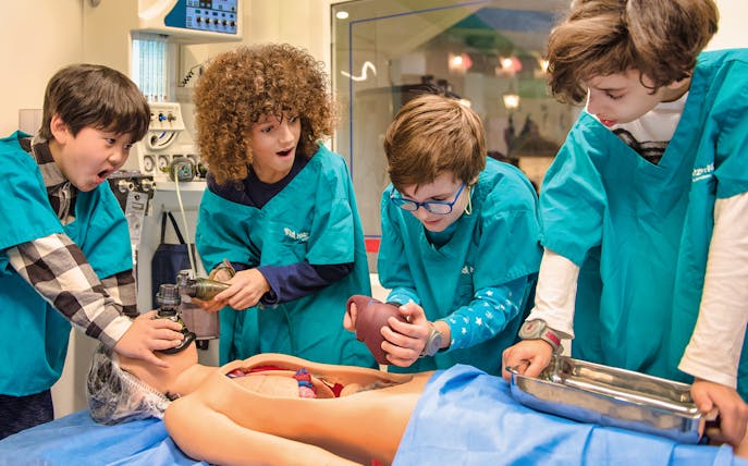 Children in medical uniforms performing a mock surgery at Kidzania.