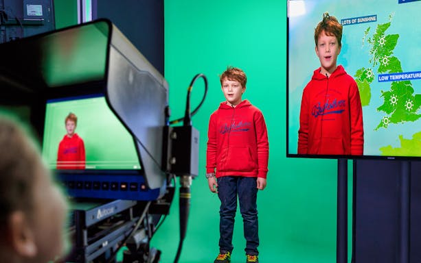 Child presenting weather forecast at KidZania on green screen.