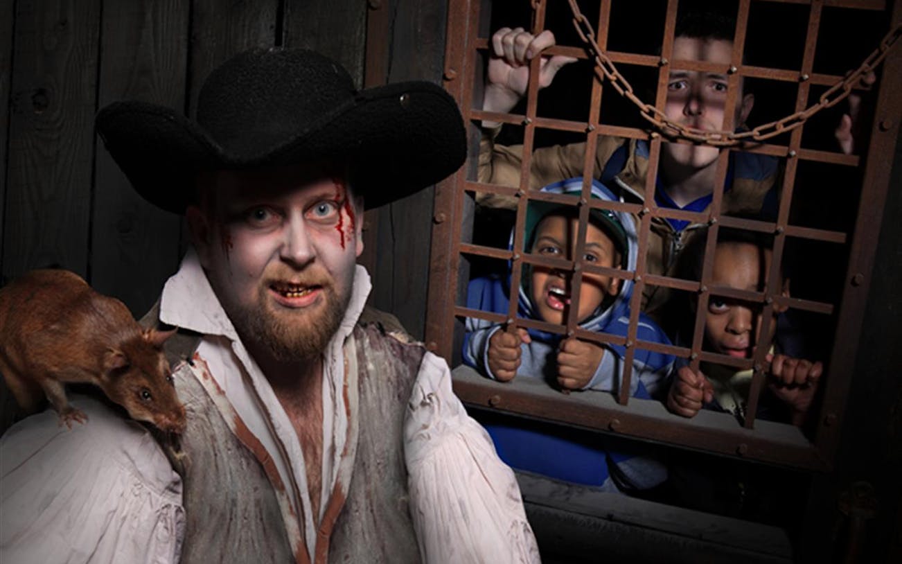 Actor in period costume with rat on shoulder, people behind bars at The London Bridge Experience.