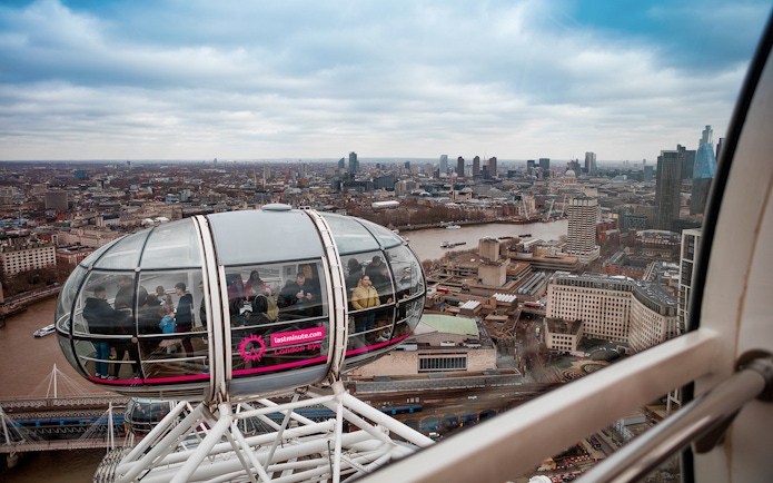 London Eye capsule with passengers overlooking the Thames River and city skyline.