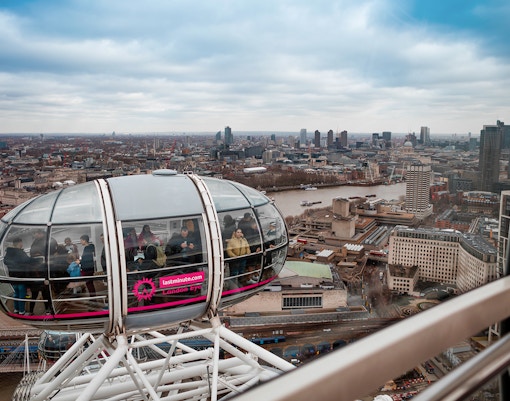 London Eye capsule with passengers overlooking the Thames River and city skyline.